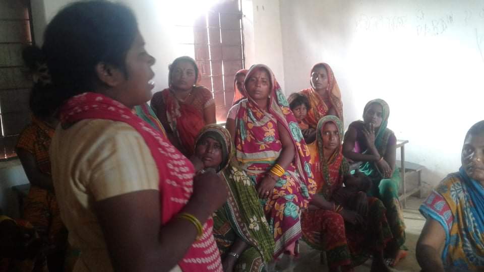 Woman talking to a group of women inside a house.